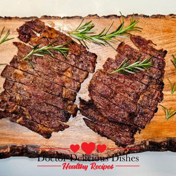 A delicious serving of thin-cut grilled ribeye steaks paired with crispy sweet potato fries and grilled corn on the cob, beautifully presented on a white plate with a rustic wooden background.