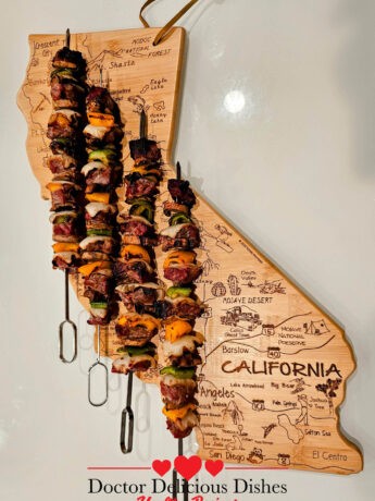 Ribeye Beef Kabab skewer with vegetables served on a california shaped wooden board.