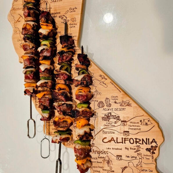 Ribeye Beef Kabab skewer with vegetables served on a california shaped wooden board.