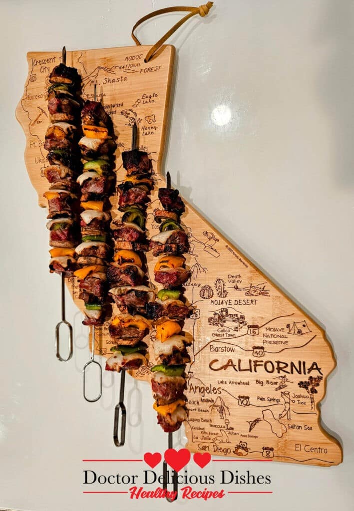 Ribeye Beef Kabab skewer with vegetables served on a california shaped wooden board.
