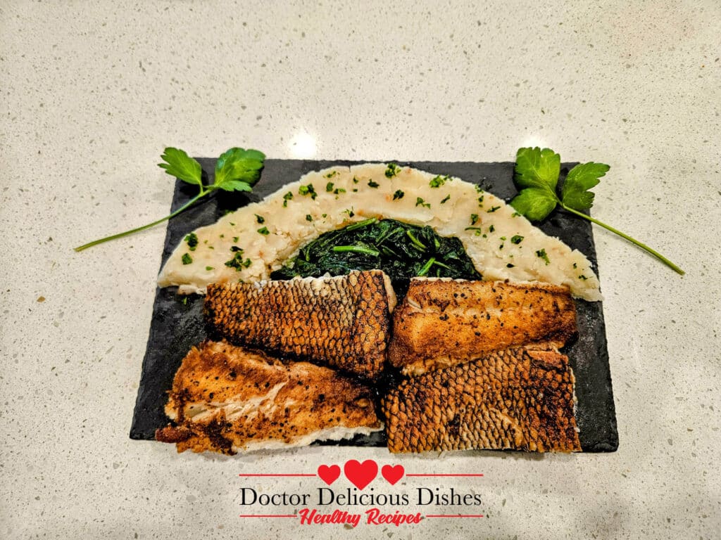 Skillet seared Chilean Sea Bass with sautéd spinash and garlic mashed potatoes served on a slate platter.