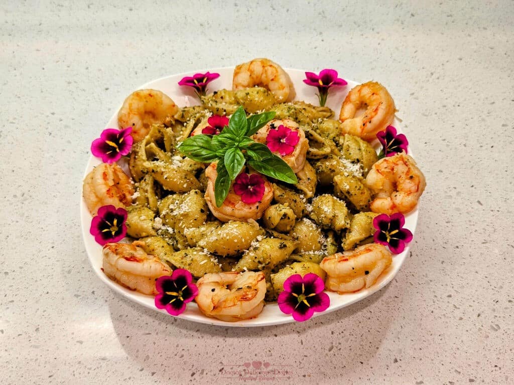 A beautifully plated dish of Almond Pesto Shrimp Pasta, garnished with shrimp, fresh basil leaves, and vibrant edible flowers, ready to be served.
