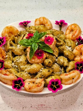 A beautifully plated dish of Almond Pesto Shrimp Pasta, garnished with shrimp, fresh basil leaves, and vibrant edible flowers, ready to be served.