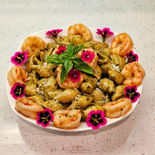 A beautifully plated dish of Almond Pesto Shrimp Pasta, garnished with shrimp, fresh basil leaves, and vibrant edible flowers, ready to be served.