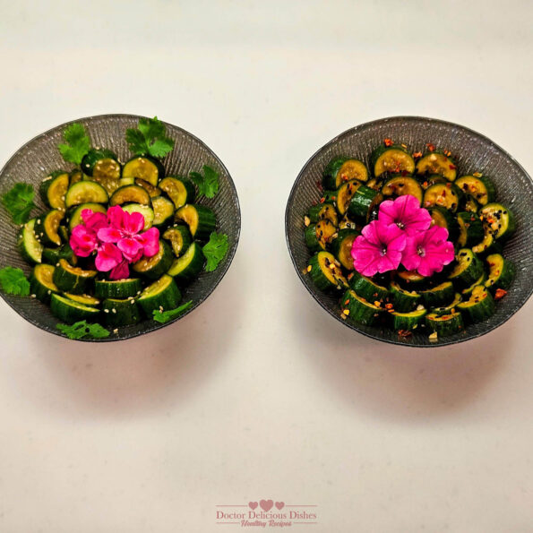 Two bowls of Chinese Cucumber Salad garnished with pink flowers and cilantro, presented side by side, with one spicy and one non-spicy version, showcasing vibrant and fresh ingredients.