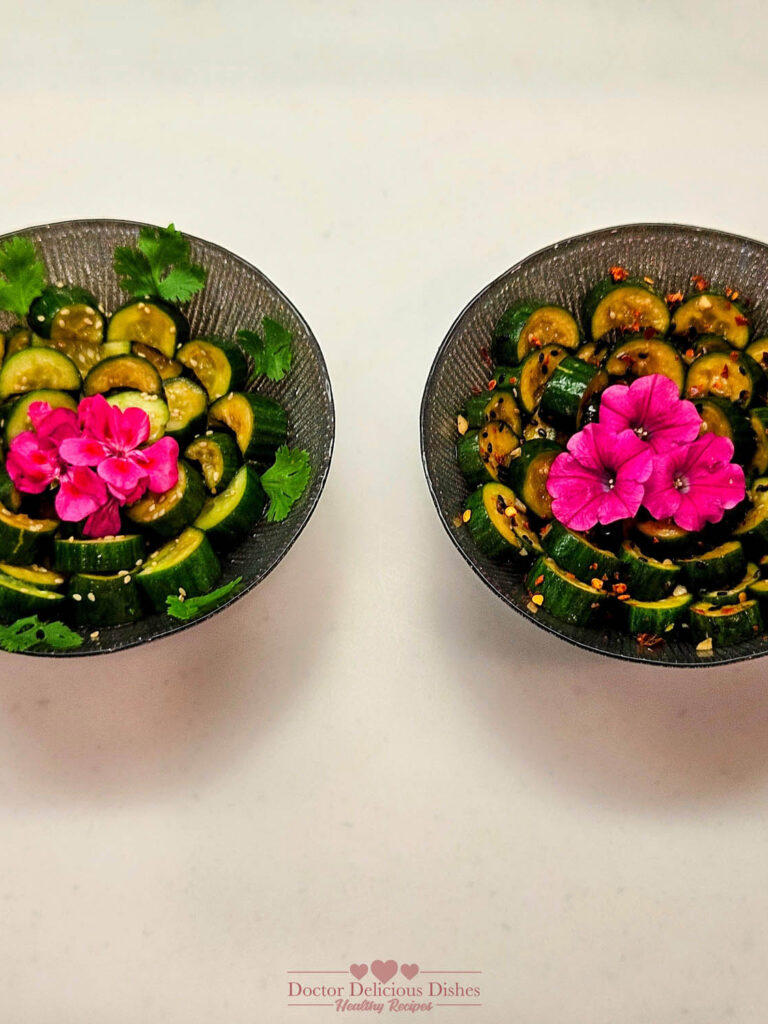 Two bowls of Chinese Cucumber Salad garnished with pink flowers and cilantro, presented side by side, with one spicy and one non-spicy version, showcasing vibrant and fresh ingredients.