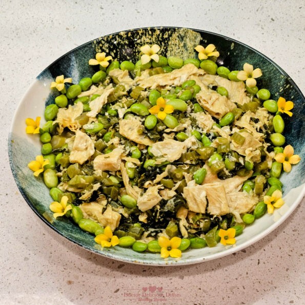 A vibrant Chinese dish featuring tofu skin, edamame, and preserved mustard greens, garnished with yellow blossoms, beautifully arranged in a blue and white asian style bowl.