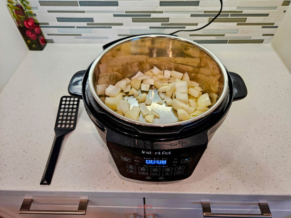 Diced onions sautéing in an Instant Pot on sauté mode, releasing aromatic flavors.