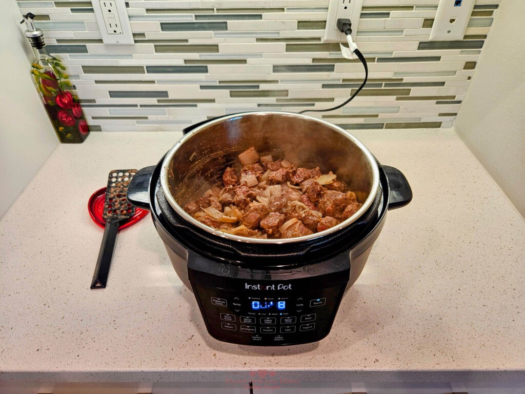 Beef cubes browning with onions in an Instant Pot, sealing in rich flavors.