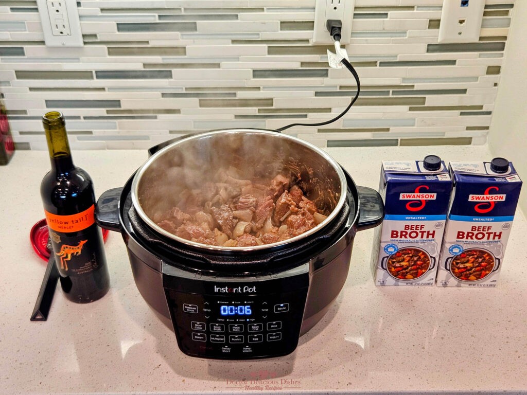 Beef and onions simmering in an Instant Pot with added beef broth and red wine for flavor.