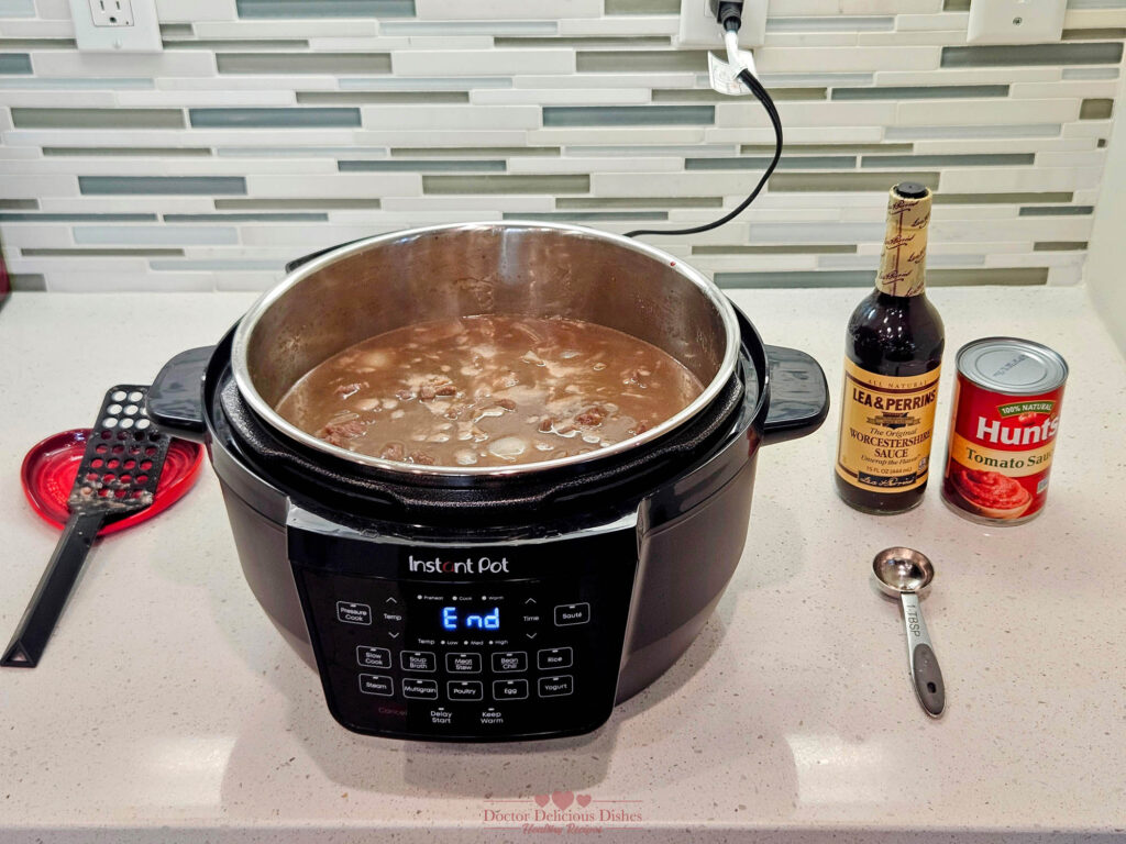 Beef stew mixture simmering in an Instant Pot with Worcestershire sauce and tomato sauce added for flavor.