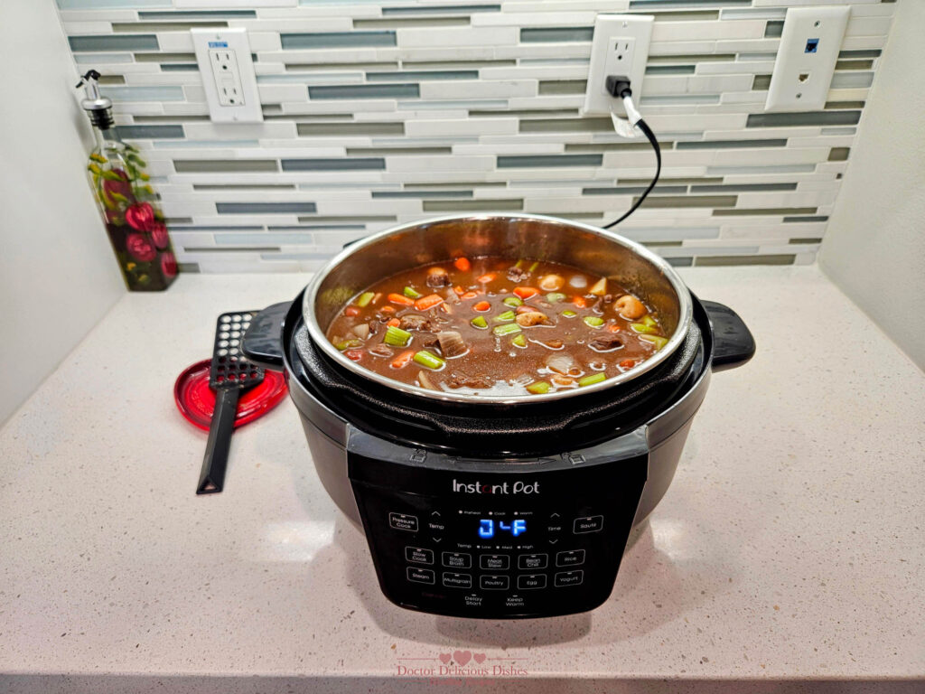 Beef stew simmering with baby potatoes, carrots, and celery inside an Instant Pot.