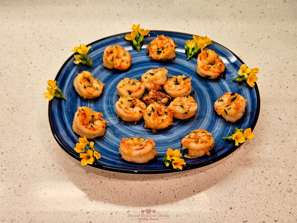 A beautifully arranged platter of Garlic Shrimp, garnished with parsley, oregano, basil and decorative yellow flowers on a blue plate.