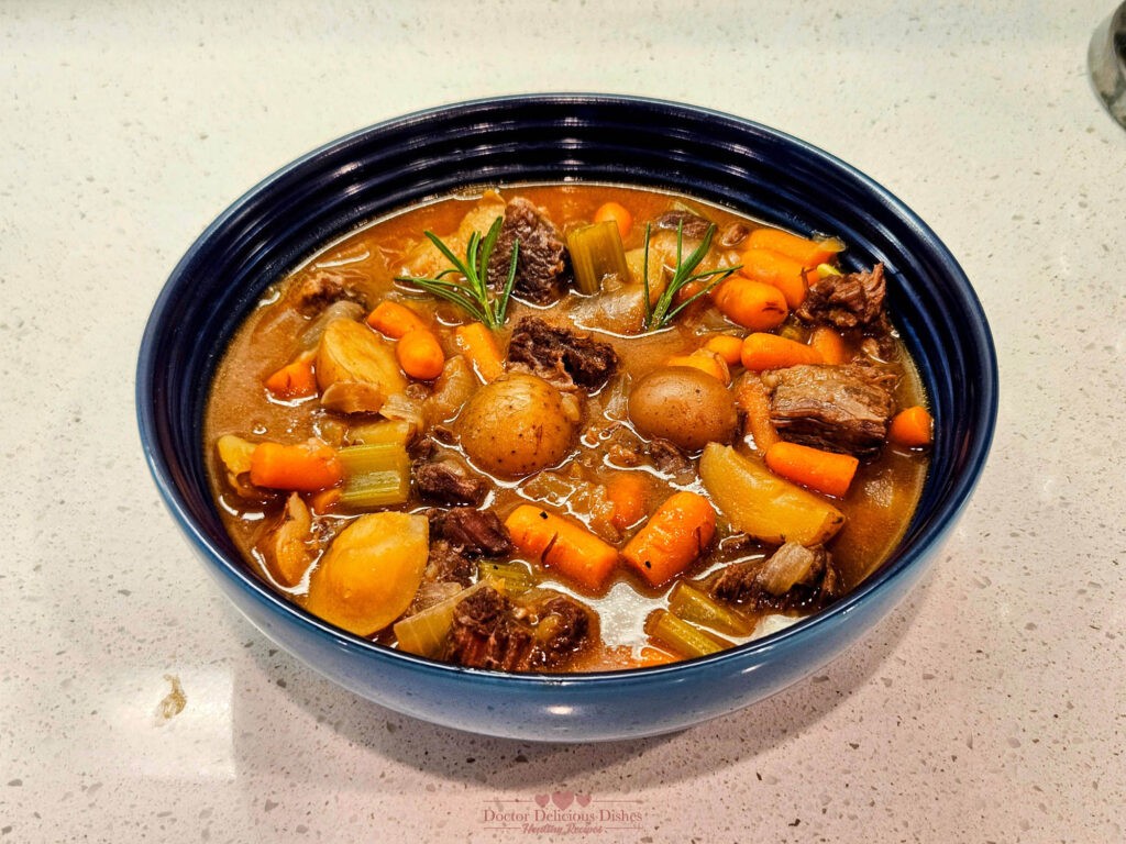 A bowl of hearty beef stew made in an Instant Pot and garnished with rosemary, featuring tender beef, potatoes, carrots, and celery in a rich broth.