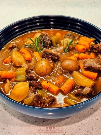 A bowl of hearty beef stew made in an Instant Pot and garnished with rosemary, featuring tender beef, potatoes, carrots, and celery in a rich broth.