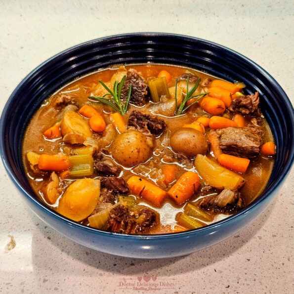 A bowl of hearty beef stew made in an Instant Pot and garnished with rosemary, featuring tender beef, potatoes, carrots, and celery in a rich broth.