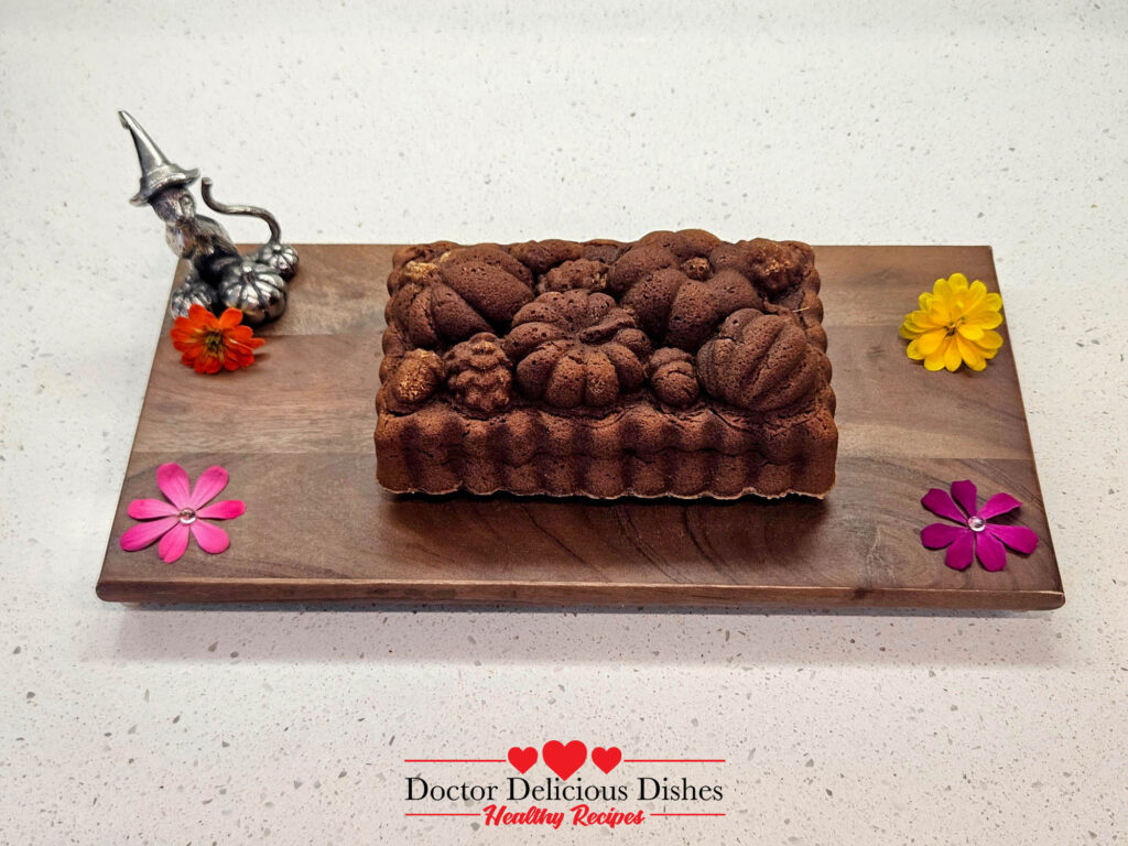 Baked Kabocha Pumpkin Cake with intricate designs from the decorative pan, placed on a wooden serving board with colorful flowers around it.