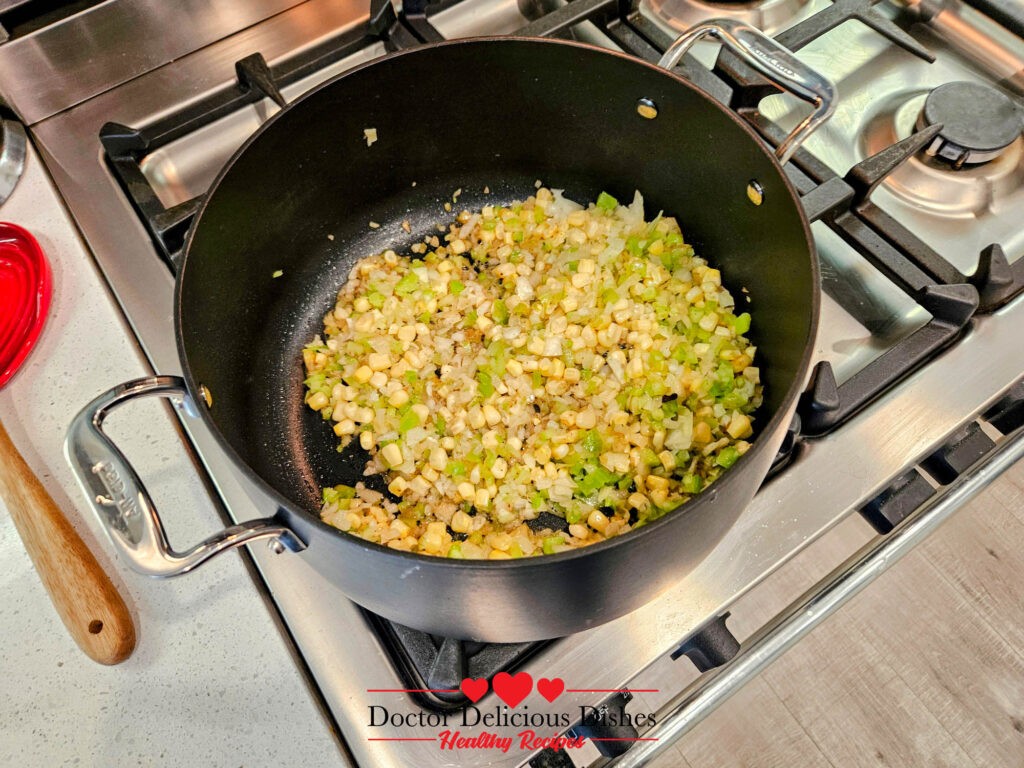 Celery, onions, and roasted corn sautéing in a black pot as part of the clam chowder recipe.