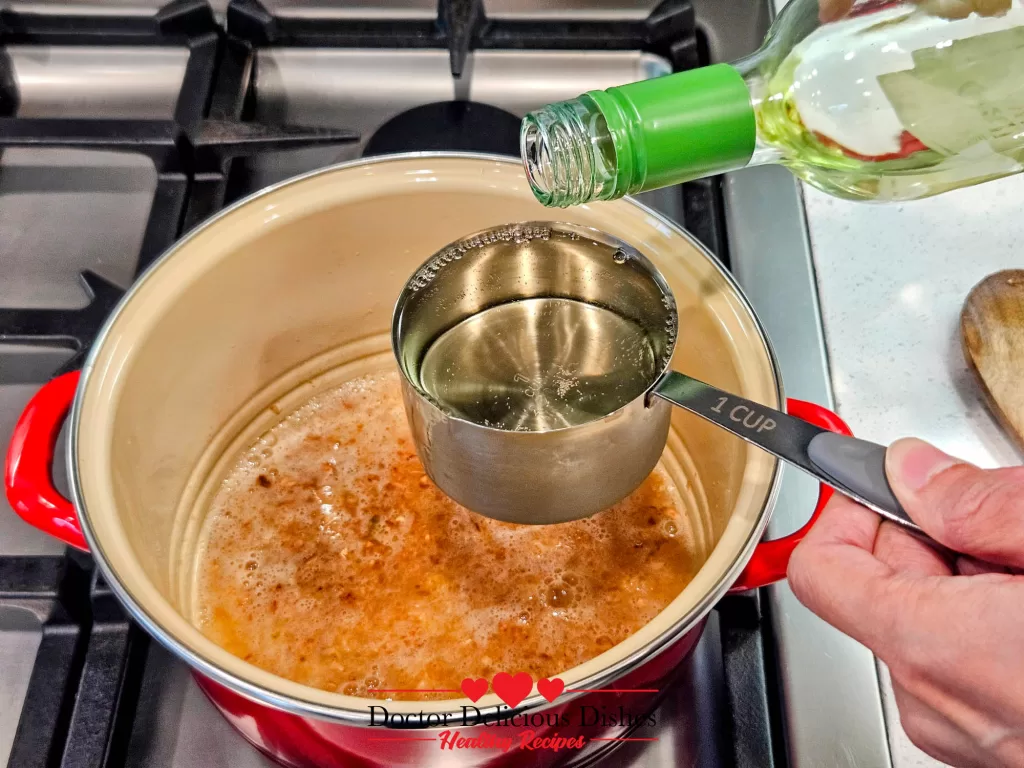 White wine being poured into a mussel pot with sautéed garlic to create the base of the broth for mussels.