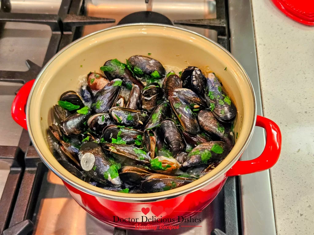 A pot of freshly steamed mussels with chopped parsley, ready to serve.