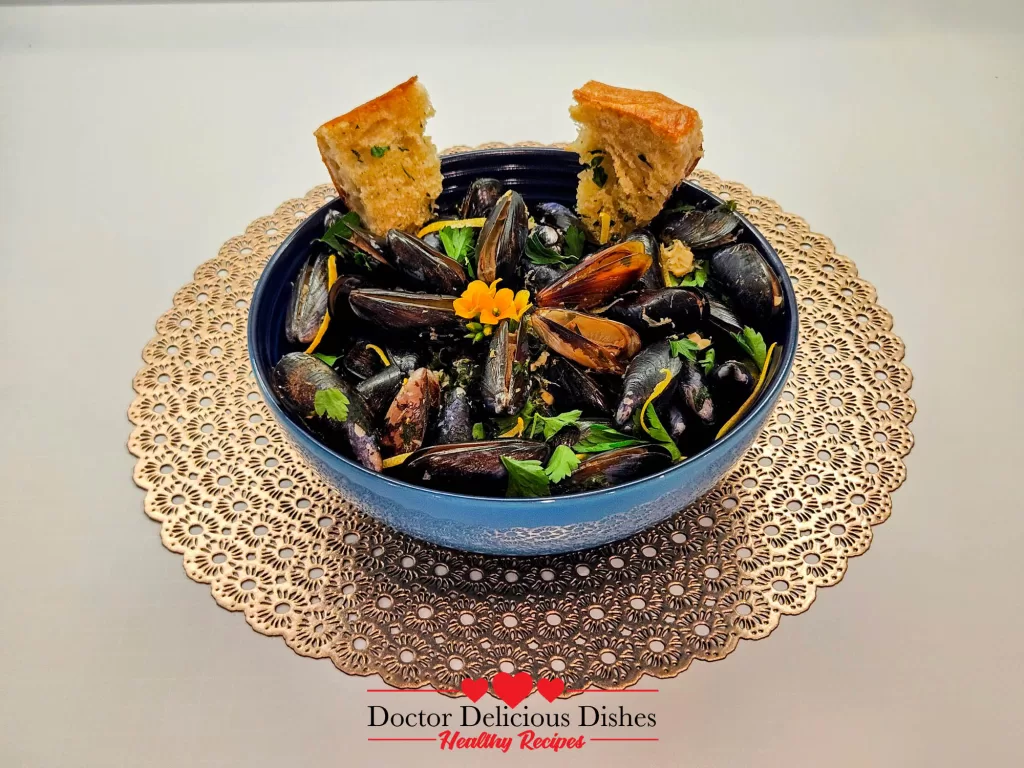 A vibrant bowl of Garlic Butter White Wine Mussels garnished with parsley and lemon zest, served with golden, crispy bread wedges on a decorative placemat.