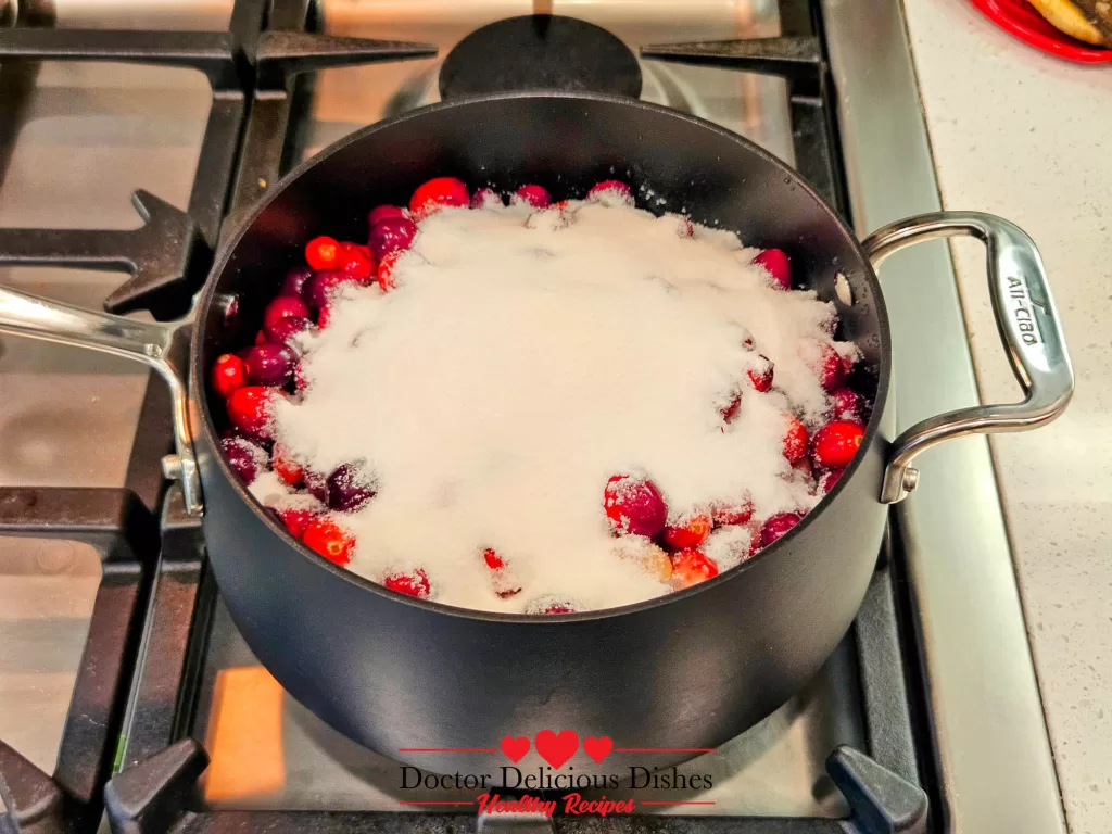 A saucepan on the stovetop with cranberries, sugar, and water combined and ready to cook.