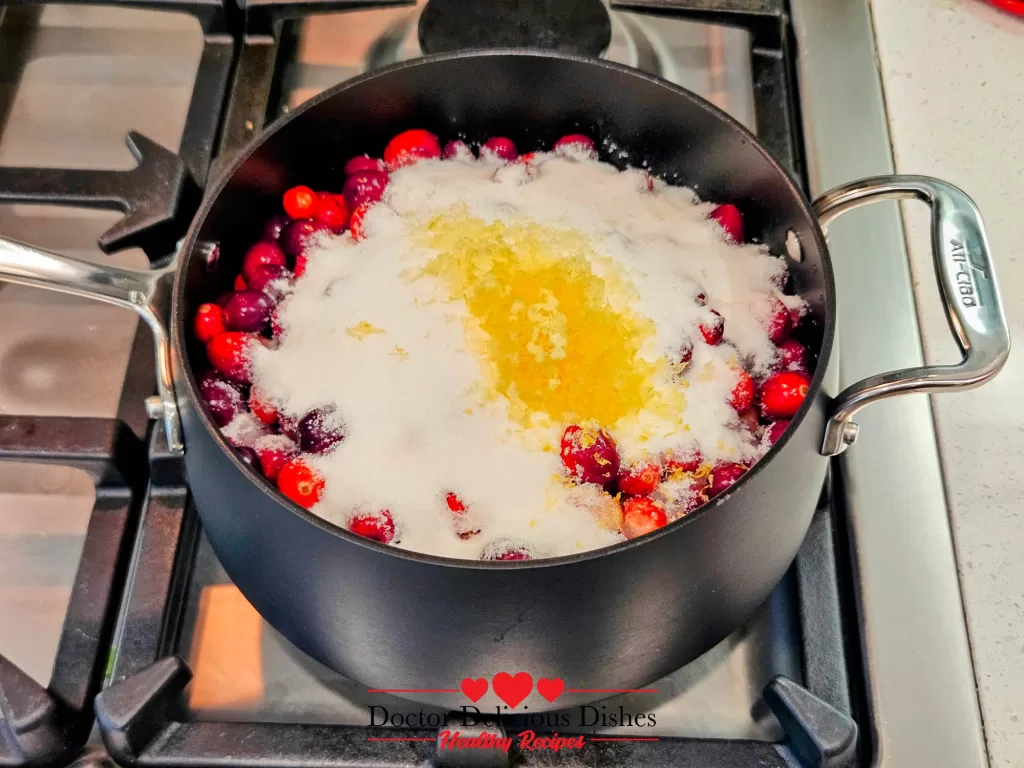 A saucepan on the stovetop with cranberries, sugar, water, and lemon zest combined and ready to cook.