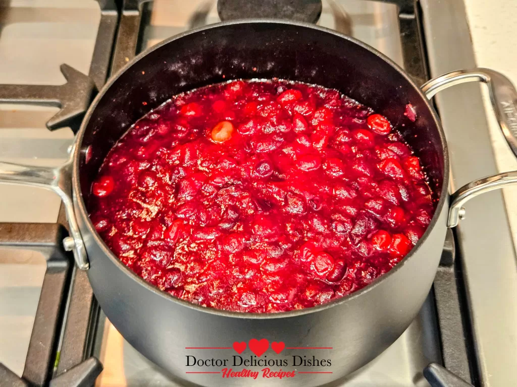 Cranberries simmering and bubbling in the saucepan as their juices release and thicken.