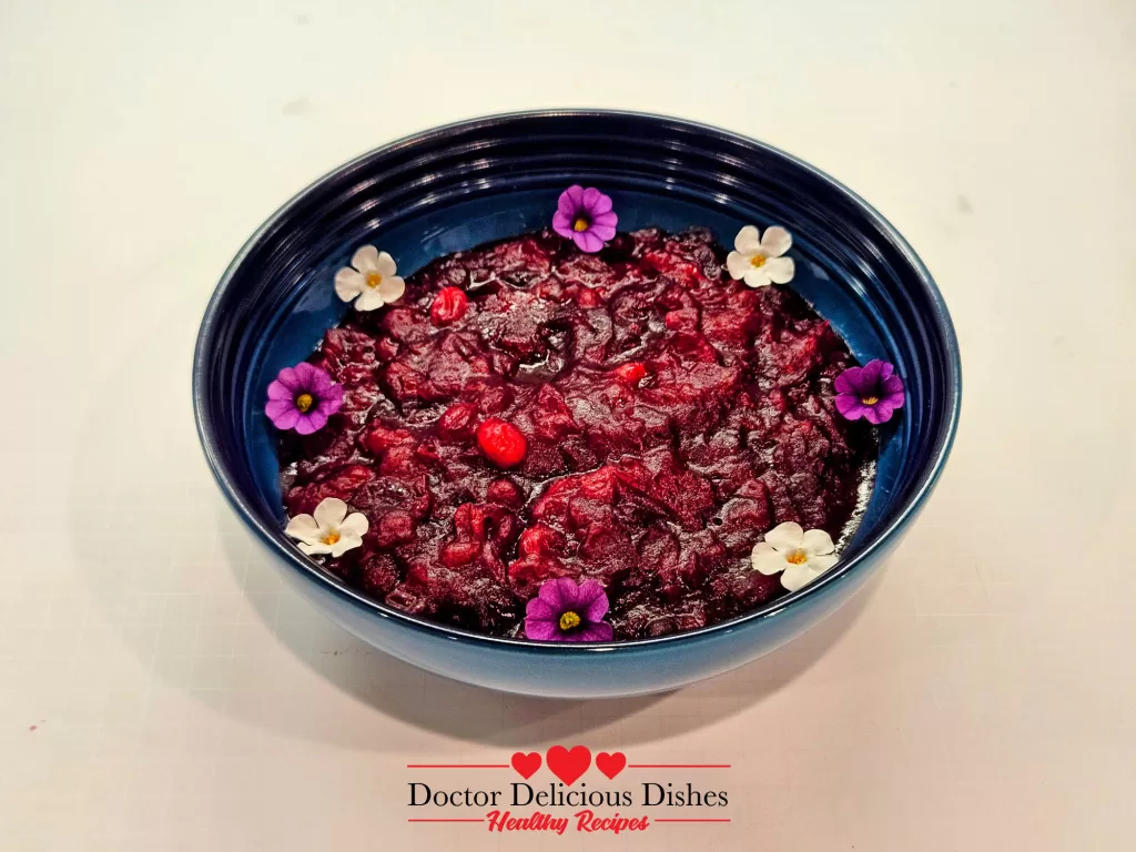 A blue Le Creuset bowl of cranberry sauce adorned with edible flowers, adding a decorative and festive touch.