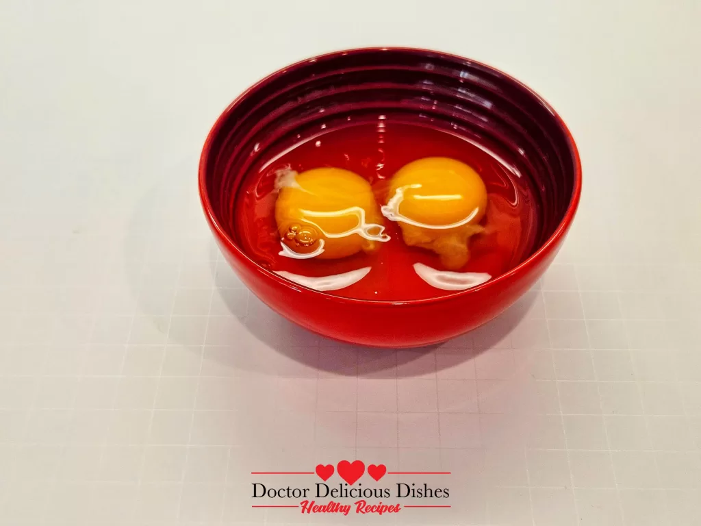 Two cracked eggs in a red bowl, showcasing their vibrant yolks.