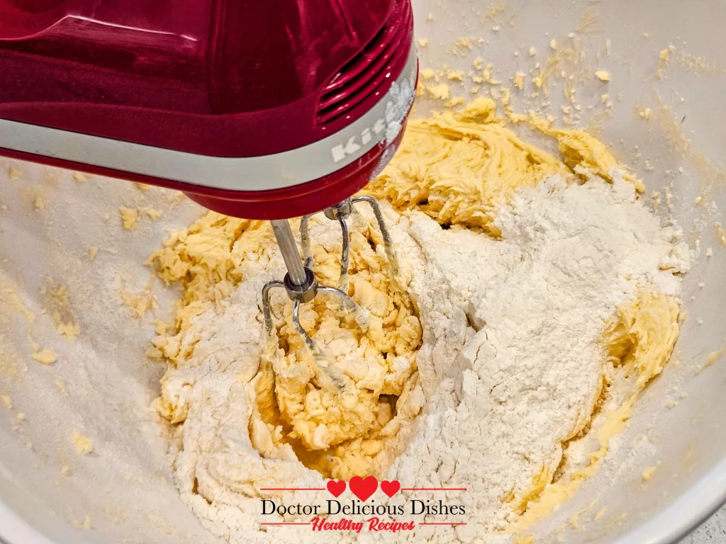 Flour being gradually added to the wet ingredients, with a mixer blending the dough.