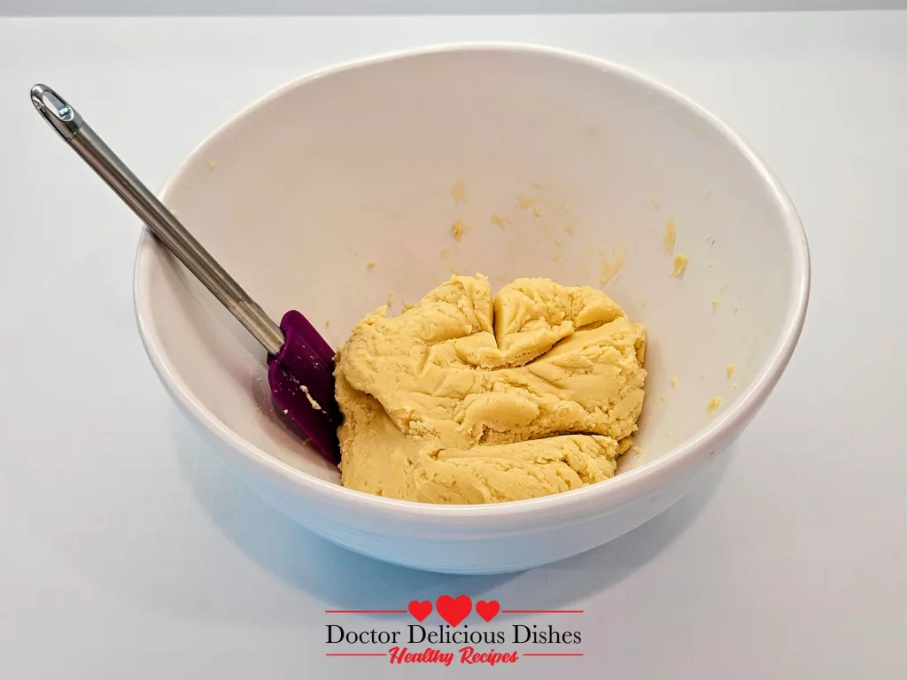 A smooth and uniform cookie dough ball in a mixing bowl, ready for rolling or chilling.