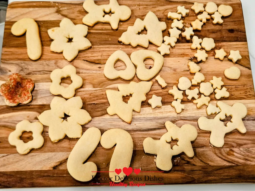 Various shapes of cut-out sugar cookies, including candy canes, snowmen, stars, and hearts, placed on a wooden board, ready for decorating.