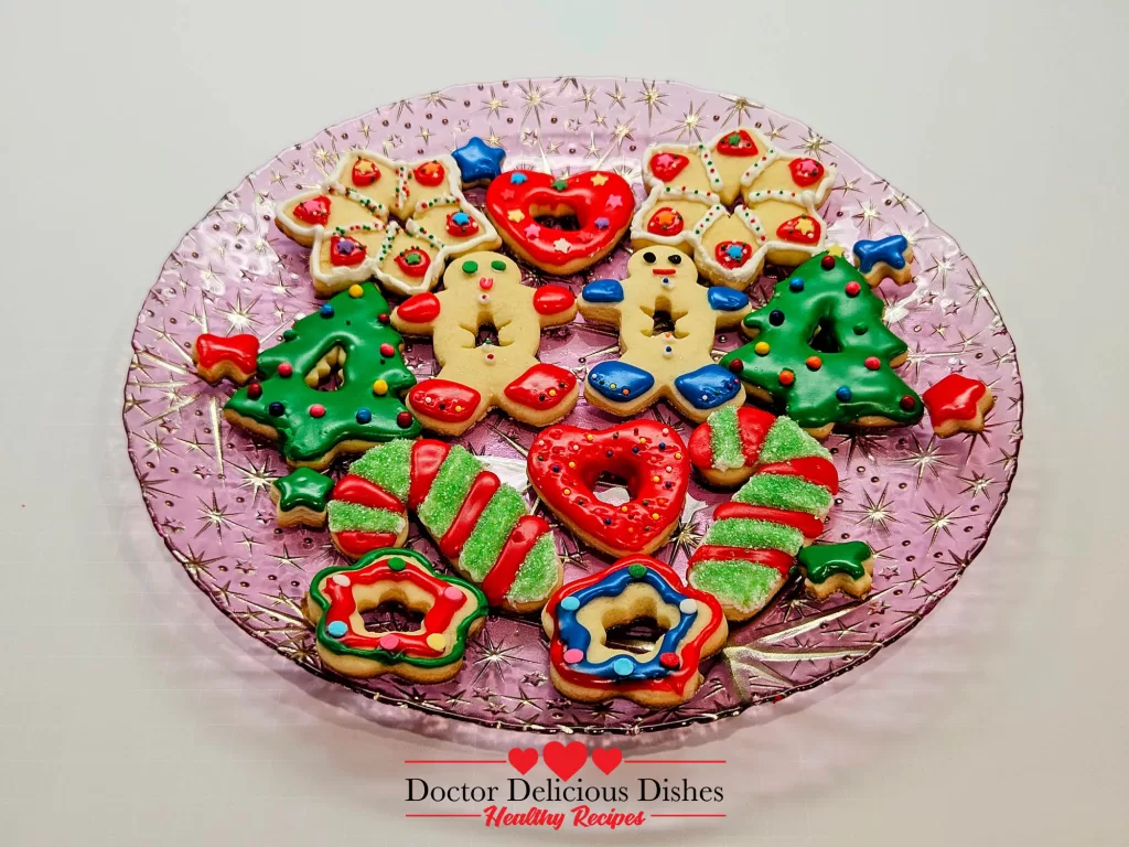 A platter of fully decorated Christmas sugar cookies in festive shapes, such as Christmas trees, snowflakes, and candy canes, placed on a glass plate with a festive pattern.