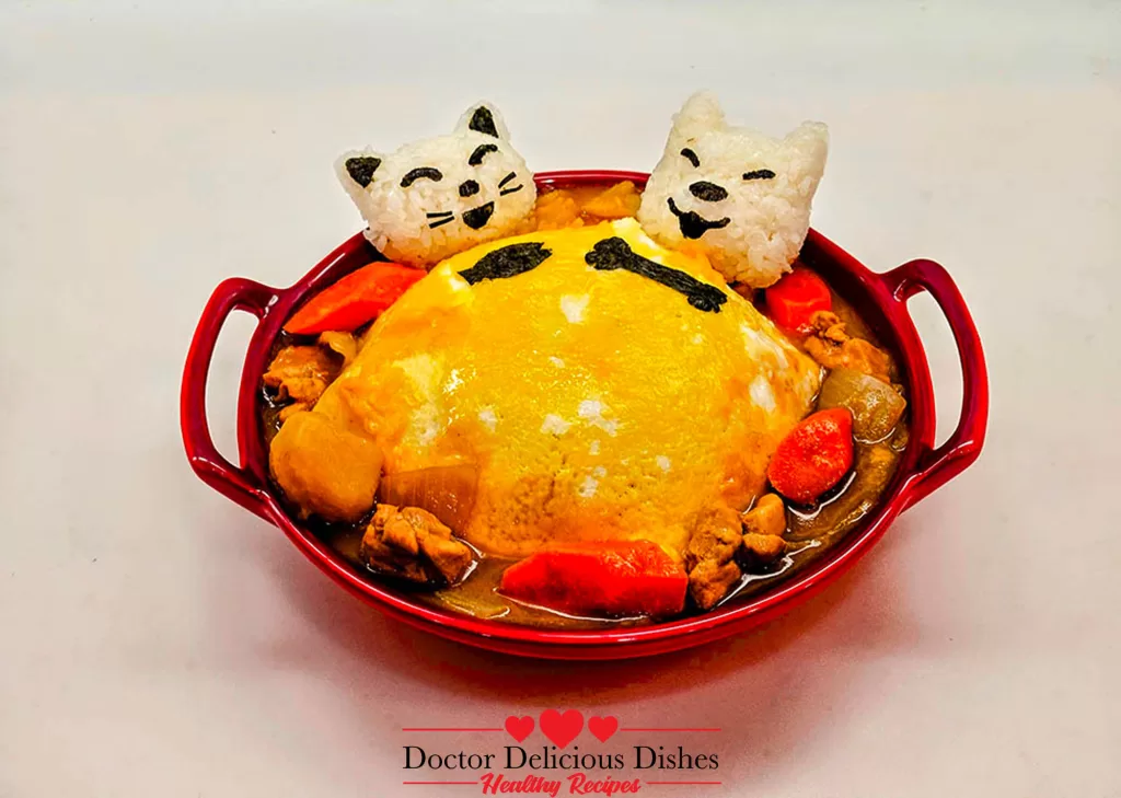 Finished dish: chicken curry with potatoes and carrots, topped with a fluffy omelet and garnished with rice shaped like cat faces, a whimsical presentation of a Japanese Chicken Curry Recipe.