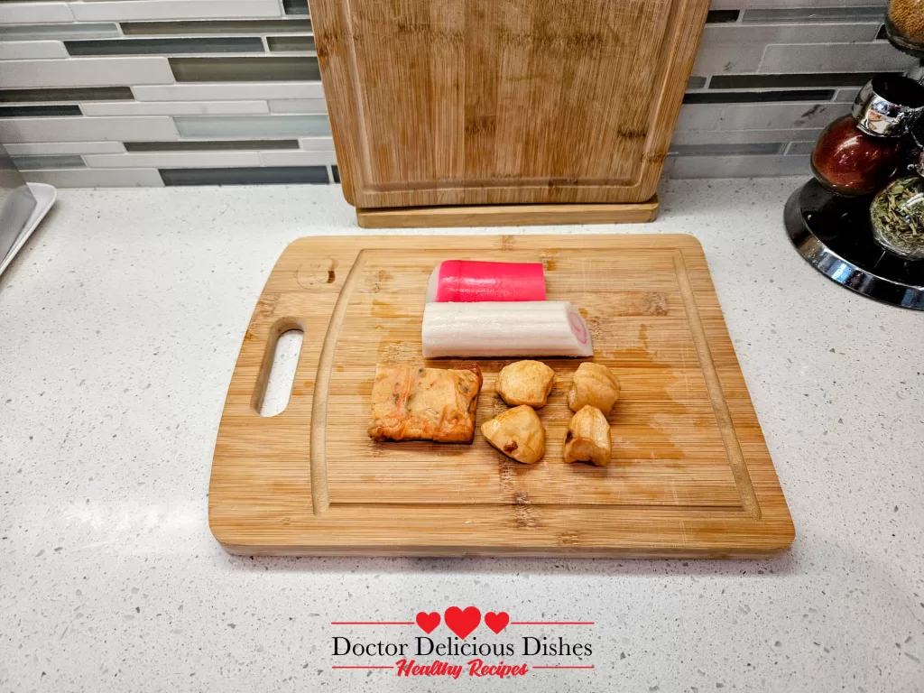 Whole fish cakes, including narutomaki and kamaboko, arranged neatly on a wooden cutting board.