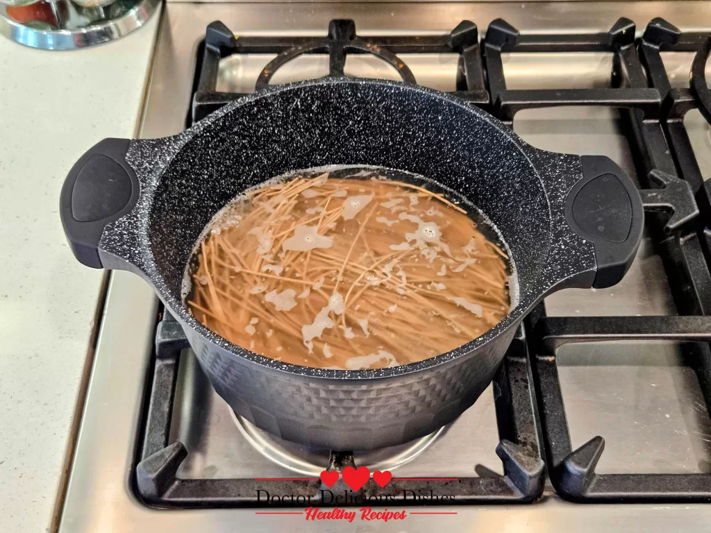 Boiling soba noodles in a black pot with frothy water, showing the cooking process.