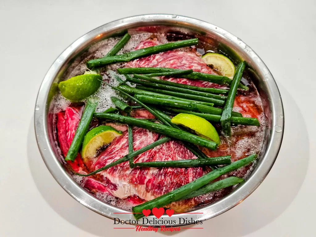 Close-up of skirt steak marinating in beer with lime wedges and green onions for air fryer skirt steak.