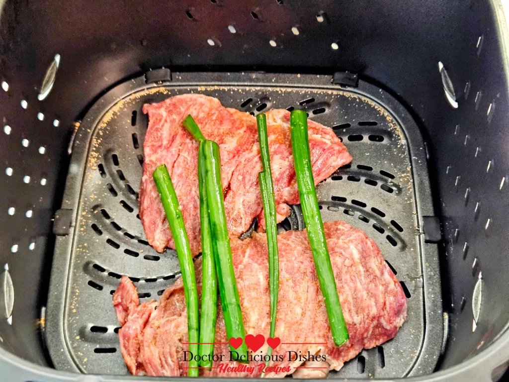 Marinated skirt steak in an air fryer basket with green onions, ready for cooking.