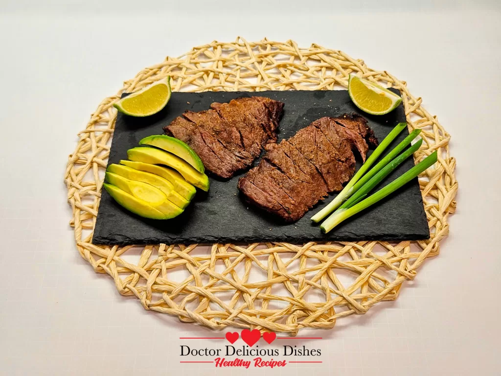 Air fryer skirt steak served with lime wedges, avocado slices, and green onions on a black slate plate.