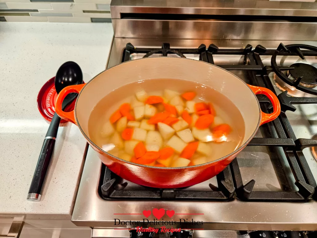 A pot of water boiling with potatoes and carrots in an orange Dutch oven, an essential step in this Japanese Chicken Curry Recipe.