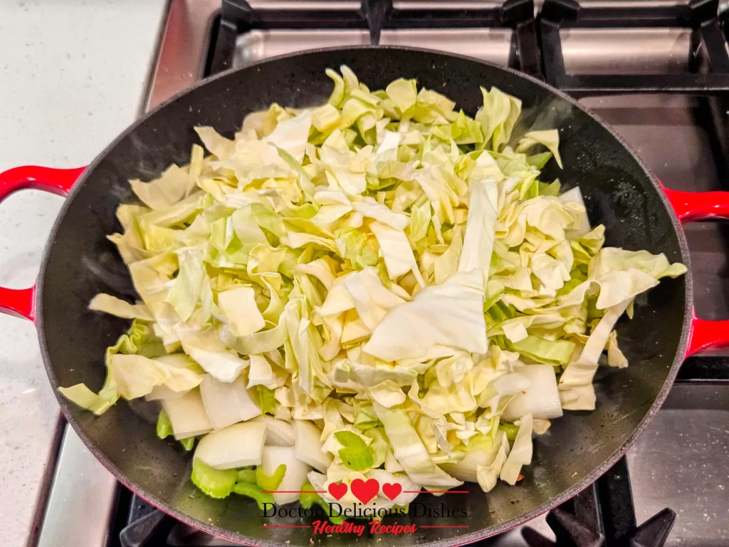 Freshly shredded cabbage added to the wok, piled on top of sautéed celery and onions, beginning to soften from the steam and heat.