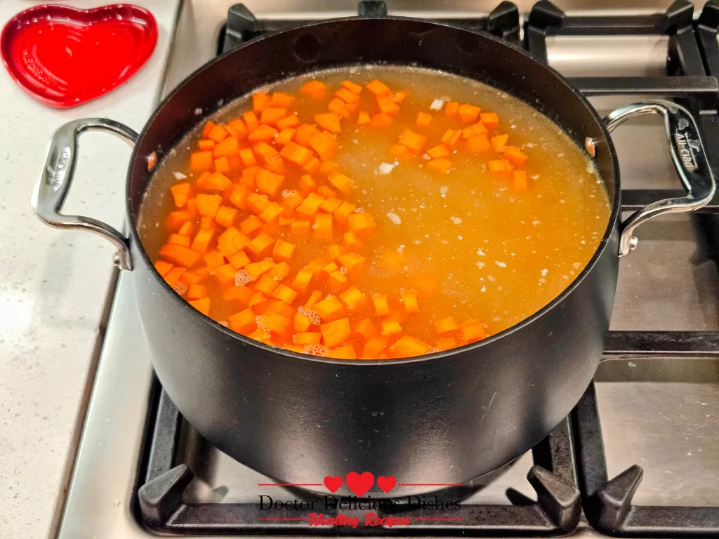 Freshly diced carrots added to the simmering chicken stock, a key step in preparing Homemade Chicken Noodle Soup with Egg Noodles.