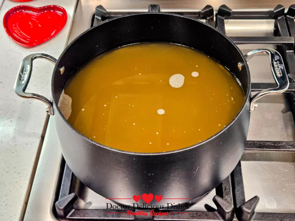 A pot filled with chicken stock simmering on the stovetop, the base for Homemade Chicken Noodle Soup with Egg Noodles.