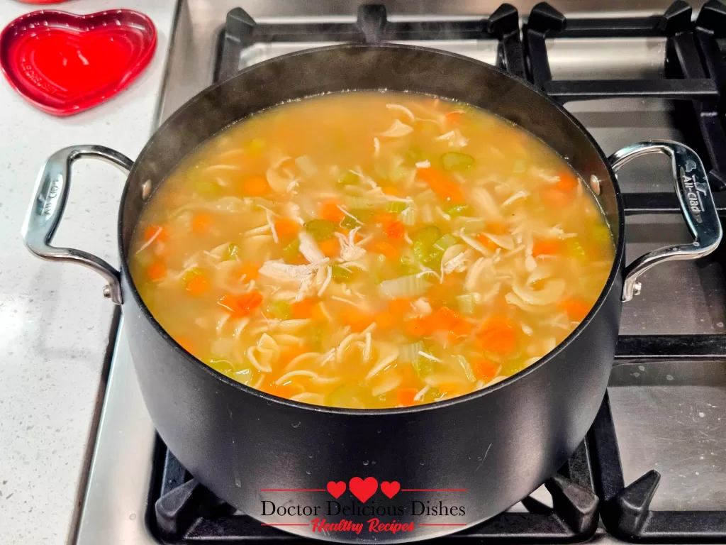 A pot of chicken noodle soup with cooked egg noodles, carrots, celery, and chicken, completing the Homemade Chicken Noodle Soup with Egg Noodles recipe.