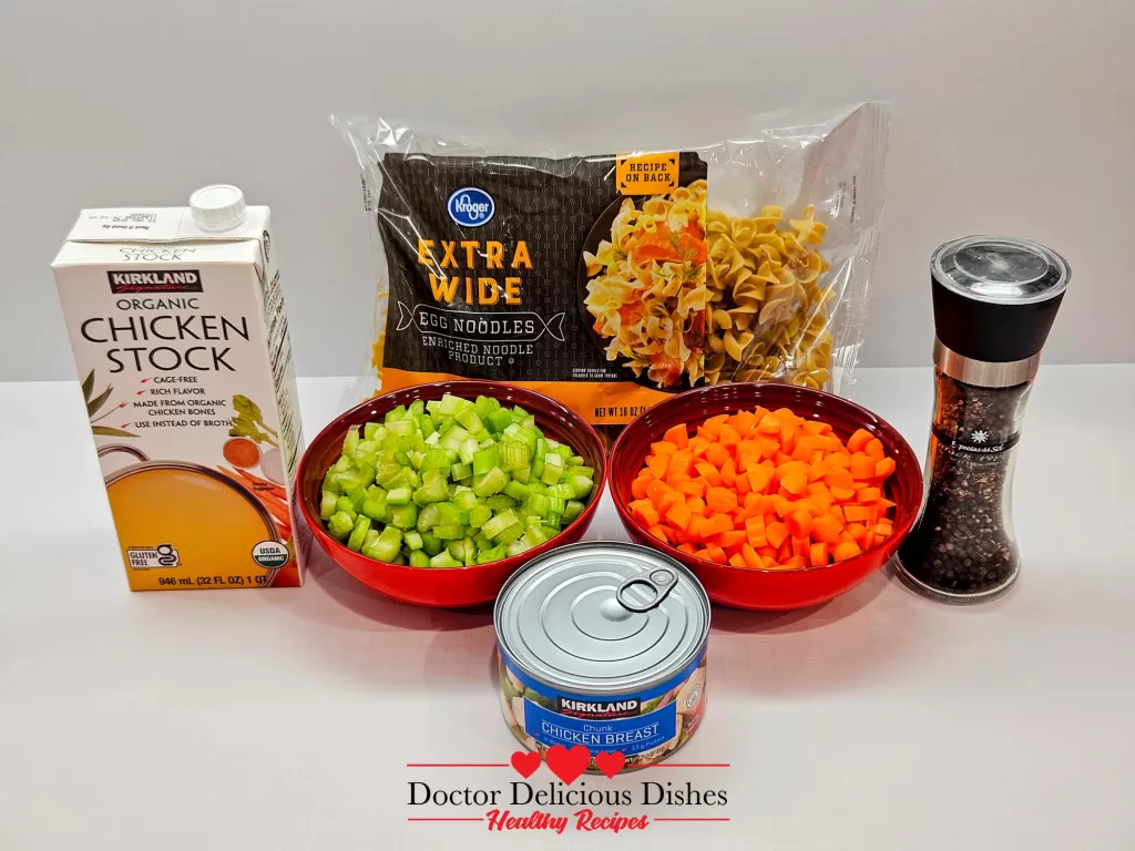 Ingredients for Homemade Chicken Noodle Soup with Egg Noodles, including chicken stock, egg noodles, chopped celery, chopped carrots, canned chicken breast, and black pepper grinder.