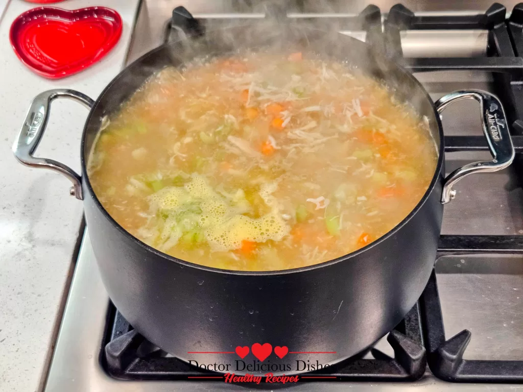 A bubbling pot of chicken soup with visible chunks of chicken, celery, and carrots, a nearly finished Homemade Chicken Noodle Soup with Egg Noodles.