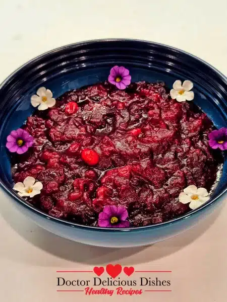 The image shows the Easy Cranberry Sauce Recipe in a blue bowl garnished with decorative edible flowers, ready to be served.