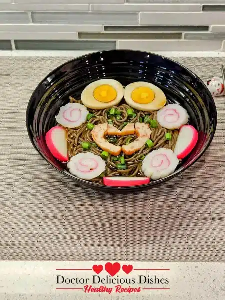 Side view of a bowl of hot soba noodle soup with traditional toppings, paired with chopsticks.