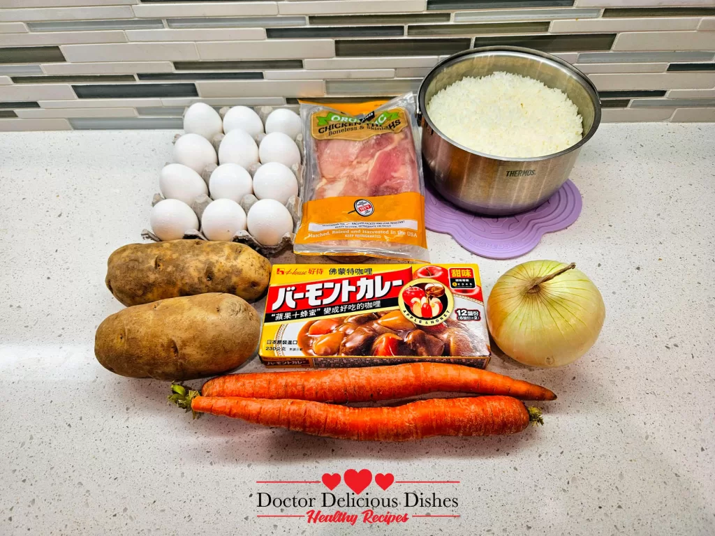 Ingredients laid out on a countertop: whole eggs, raw chicken thighs, rice in a metal pot, large russet potatoes, carrots, an onion, and a box of curry roux, perfect for making a Japanese Chicken Curry Recipe.